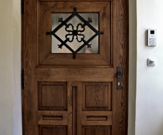 Dveře vstupní jednokřídlé v rámové zárubni, dveřní křídlo kazetové s okénkem a původní kovanou mříží, napodobení původních historických dveří, nátěr lazurou.